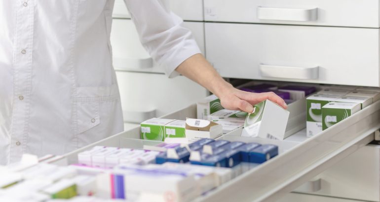Pharmacist holding medicine box and capsule pack in pharmacy drugstore.